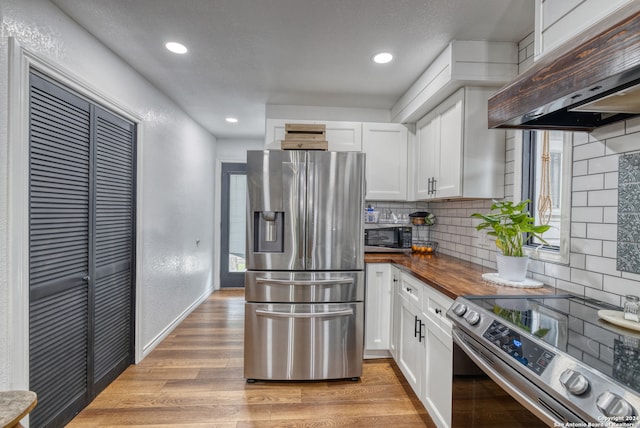 kitchen with appliances with stainless steel finishes, light hardwood / wood-style flooring, white cabinets, decorative backsplash, and exhaust hood