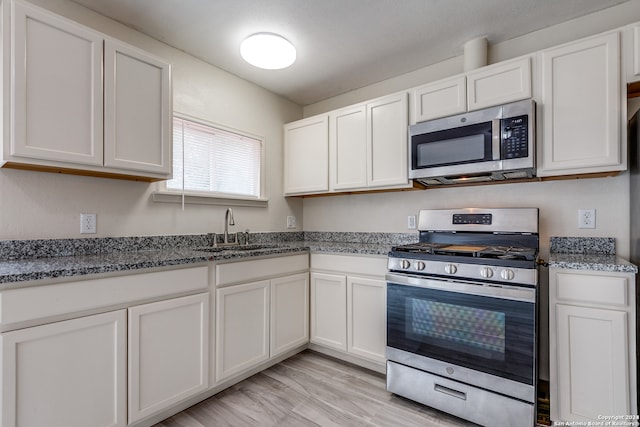 kitchen featuring stainless steel appliances, stone counters, white cabinets, and sink