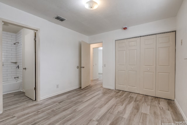 unfurnished bedroom featuring ensuite bath, a closet, light hardwood / wood-style flooring, and a textured ceiling