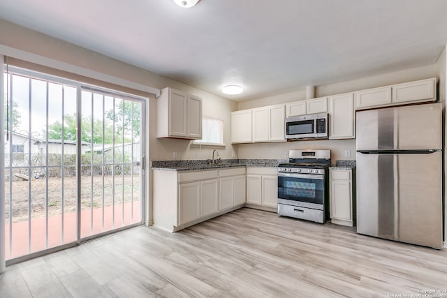 kitchen featuring stainless steel appliances, dark stone counters, white cabinetry, sink, and light hardwood / wood-style floors