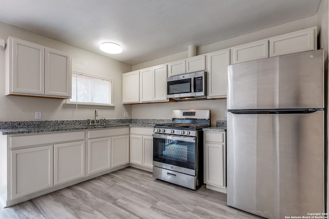 kitchen featuring dark stone counters, light wood-type flooring, appliances with stainless steel finishes, sink, and white cabinets