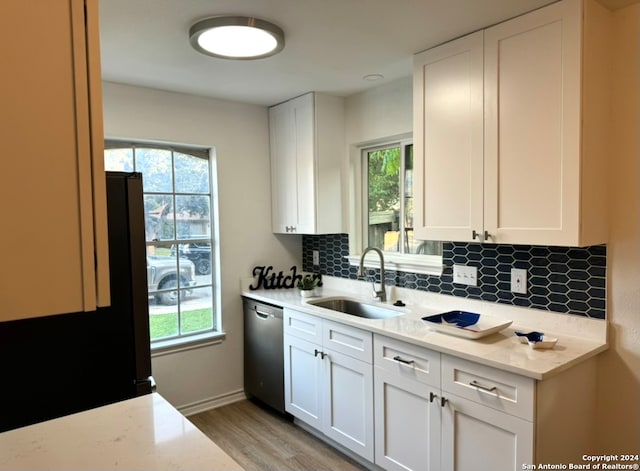 kitchen with stainless steel dishwasher, a wealth of natural light, sink, and white cabinets