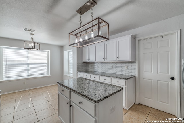 kitchen with tasteful backsplash, light tile patterned flooring, a kitchen island, hanging light fixtures, and white cabinets