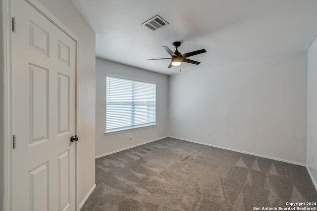 spare room featuring a textured ceiling, dark colored carpet, and ceiling fan