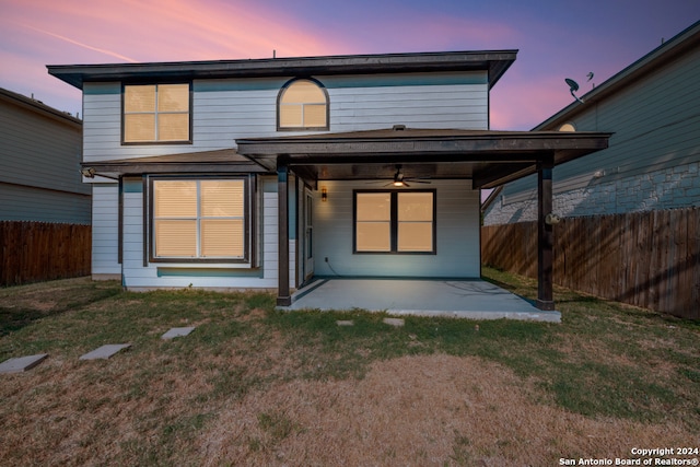 back house at dusk featuring a lawn, ceiling fan, and a patio area