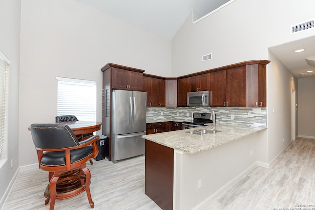 kitchen with light stone counters, appliances with stainless steel finishes, high vaulted ceiling, sink, and kitchen peninsula