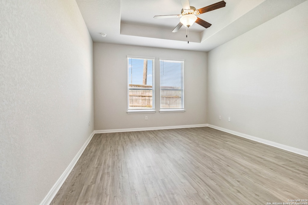 spare room with light hardwood / wood-style floors, ceiling fan, and a raised ceiling