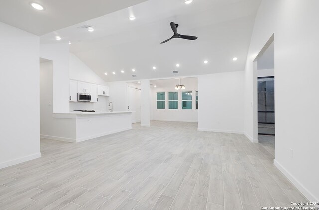 unfurnished living room with ceiling fan with notable chandelier, light hardwood / wood-style flooring, sink, and high vaulted ceiling