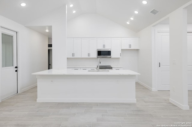 kitchen with white cabinetry, lofted ceiling, and an island with sink