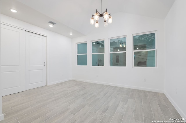 spare room with an inviting chandelier, vaulted ceiling, and light hardwood / wood-style floors