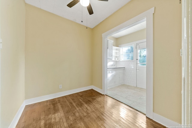 unfurnished room featuring tile walls, hardwood / wood-style flooring, and ceiling fan