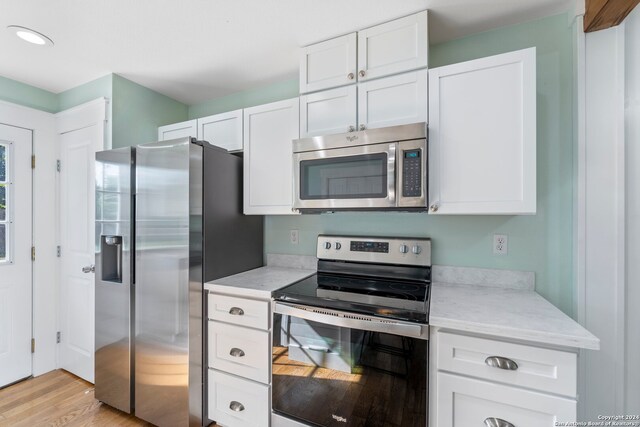 kitchen with light hardwood / wood-style floors, white cabinetry, light stone counters, and appliances with stainless steel finishes