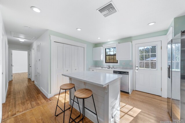 kitchen featuring white cabinetry, sink, stainless steel dishwasher, a center island, and light wood-type flooring