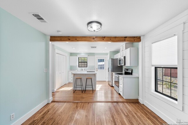 kitchen with stainless steel appliances, a kitchen island, light wood-type flooring, a kitchen bar, and white cabinets