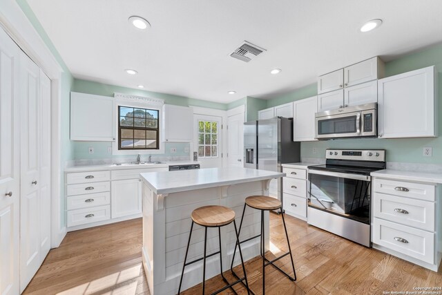 kitchen featuring white cabinetry, light wood-type flooring, stainless steel appliances, and a kitchen island