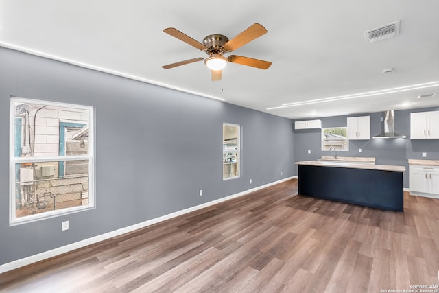 kitchen with white cabinets, wall chimney range hood, plenty of natural light, and wood-type flooring