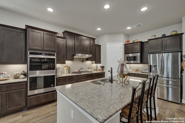 kitchen with light stone countertops, sink, a kitchen island with sink, and appliances with stainless steel finishes