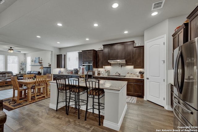 kitchen with stainless steel appliances, light hardwood / wood-style floors, a breakfast bar area, ceiling fan, and a kitchen island with sink