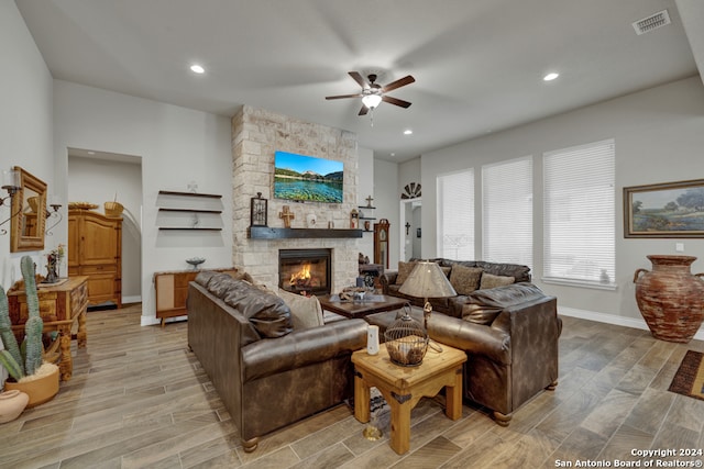 living room with ceiling fan, a stone fireplace, and light hardwood / wood-style flooring