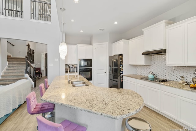 kitchen with a kitchen bar, light hardwood / wood-style floors, black appliances, and hanging light fixtures