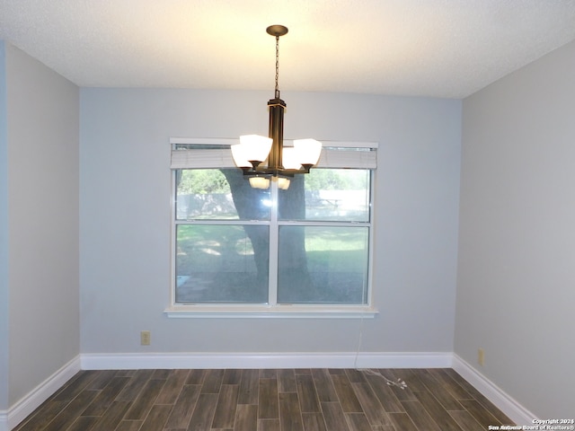 empty room featuring dark hardwood / wood-style floors, a textured ceiling, and a chandelier