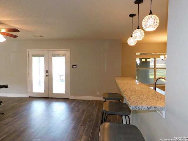 kitchen featuring french doors, hanging light fixtures, a textured ceiling, dark hardwood / wood-style floors, and a breakfast bar