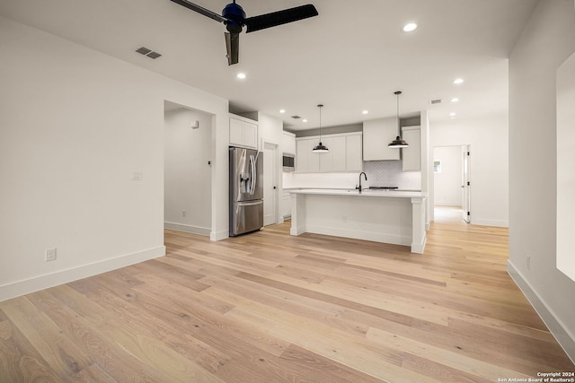 kitchen featuring white cabinetry, appliances with stainless steel finishes, hanging light fixtures, a kitchen island with sink, and light hardwood / wood-style flooring