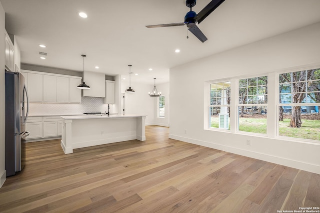 kitchen with an island with sink, white cabinetry, pendant lighting, and stainless steel refrigerator