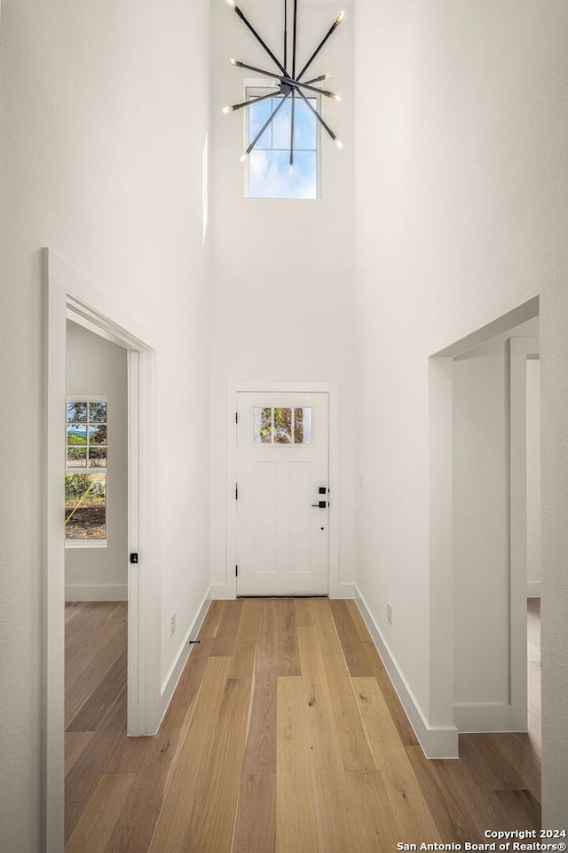 entryway with light hardwood / wood-style floors, a chandelier, and a towering ceiling