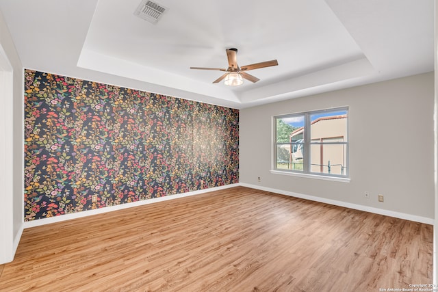 spare room with light hardwood / wood-style flooring, ceiling fan, and a raised ceiling