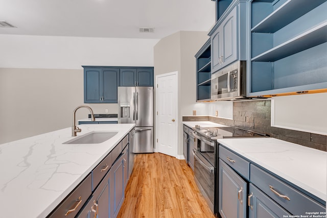 kitchen with sink, appliances with stainless steel finishes, light stone countertops, blue cabinets, and light wood-type flooring