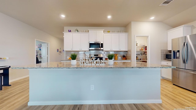 kitchen with backsplash, appliances with stainless steel finishes, light wood-type flooring, white cabinets, and a kitchen island with sink