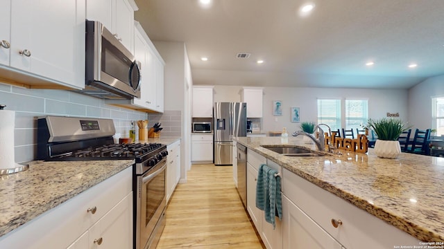 kitchen featuring stainless steel appliances, white cabinetry, light stone countertops, sink, and light hardwood / wood-style flooring