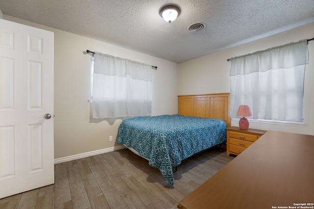 bedroom featuring a textured ceiling, hardwood / wood-style floors, and multiple windows