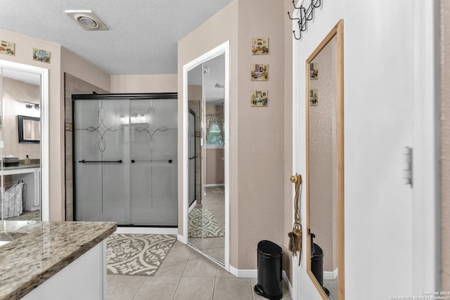 bathroom with an enclosed shower, vanity, a textured ceiling, and tile patterned flooring