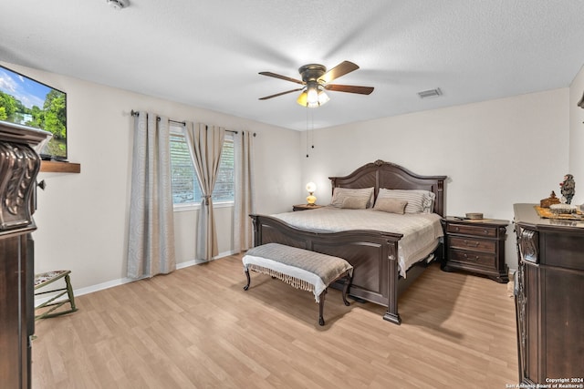 bedroom featuring light hardwood / wood-style floors, ceiling fan, and a textured ceiling