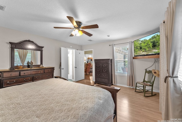 bedroom featuring ceiling fan, multiple windows, light wood-type flooring, and a textured ceiling