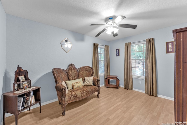 living area with a textured ceiling, ceiling fan, and light hardwood / wood-style flooring