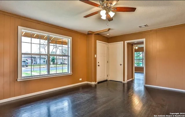 unfurnished room with ceiling fan, a textured ceiling, wooden walls, and dark hardwood / wood-style flooring