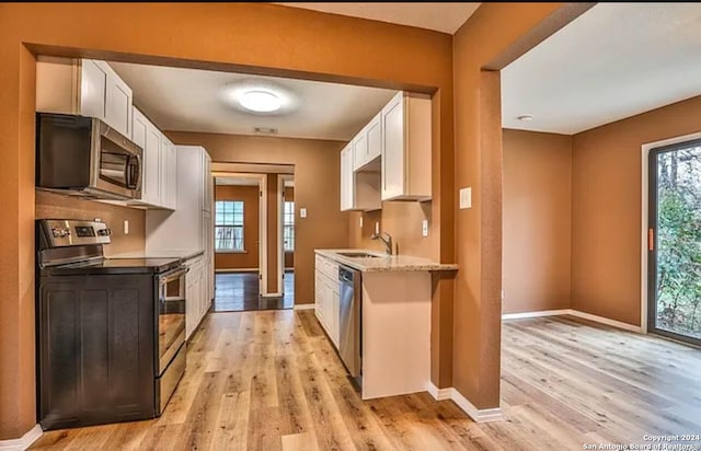 kitchen with white cabinets, stainless steel appliances, light hardwood / wood-style floors, and light stone counters