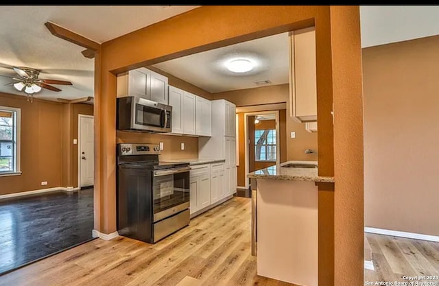 kitchen featuring light stone counters, appliances with stainless steel finishes, ceiling fan, light hardwood / wood-style flooring, and white cabinets