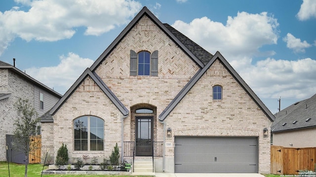 french country inspired facade with brick siding, fence, a garage, and concrete driveway