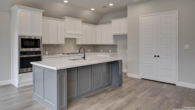 kitchen featuring appliances with stainless steel finishes, a sink, light wood-style floors, tasteful backsplash, and recessed lighting