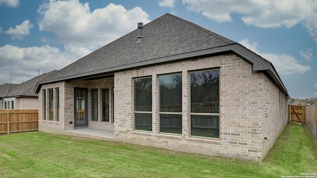 rear view of property with a patio, a fenced backyard, brick siding, a shingled roof, and a lawn