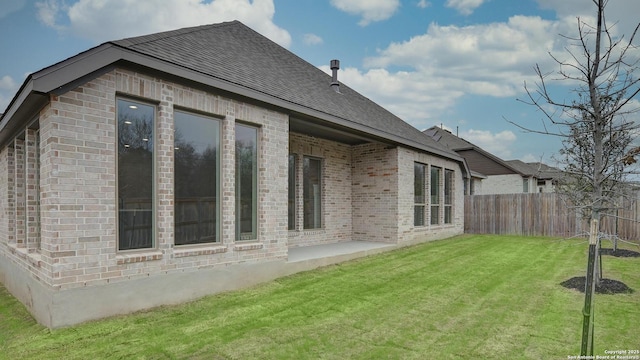 rear view of property with a yard, brick siding, a shingled roof, and fence