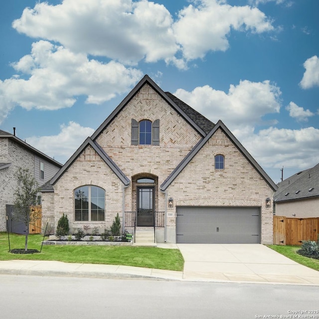 french country inspired facade with a garage, brick siding, fence, concrete driveway, and a front yard