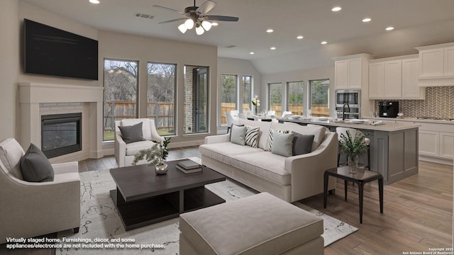living area with recessed lighting, light wood-type flooring, a brick fireplace, a ceiling fan, and vaulted ceiling