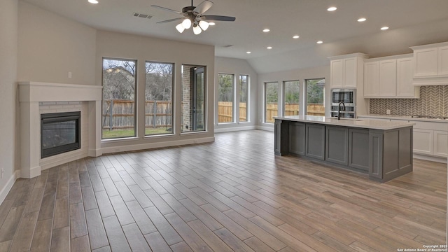 kitchen featuring open floor plan, stainless steel appliances, light countertops, backsplash, and white cabinetry