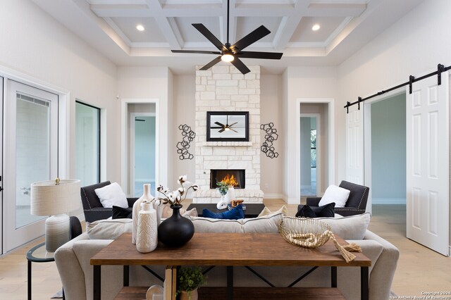 living room with beam ceiling, a fireplace, light hardwood / wood-style flooring, coffered ceiling, and a barn door