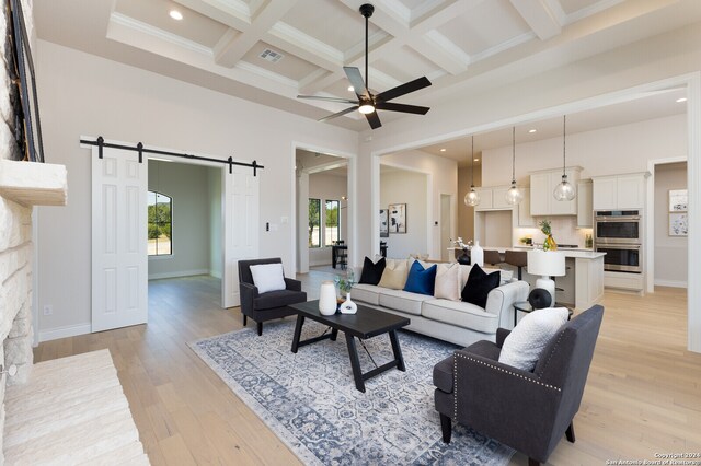 living room with a barn door, coffered ceiling, ceiling fan, beam ceiling, and light hardwood / wood-style flooring